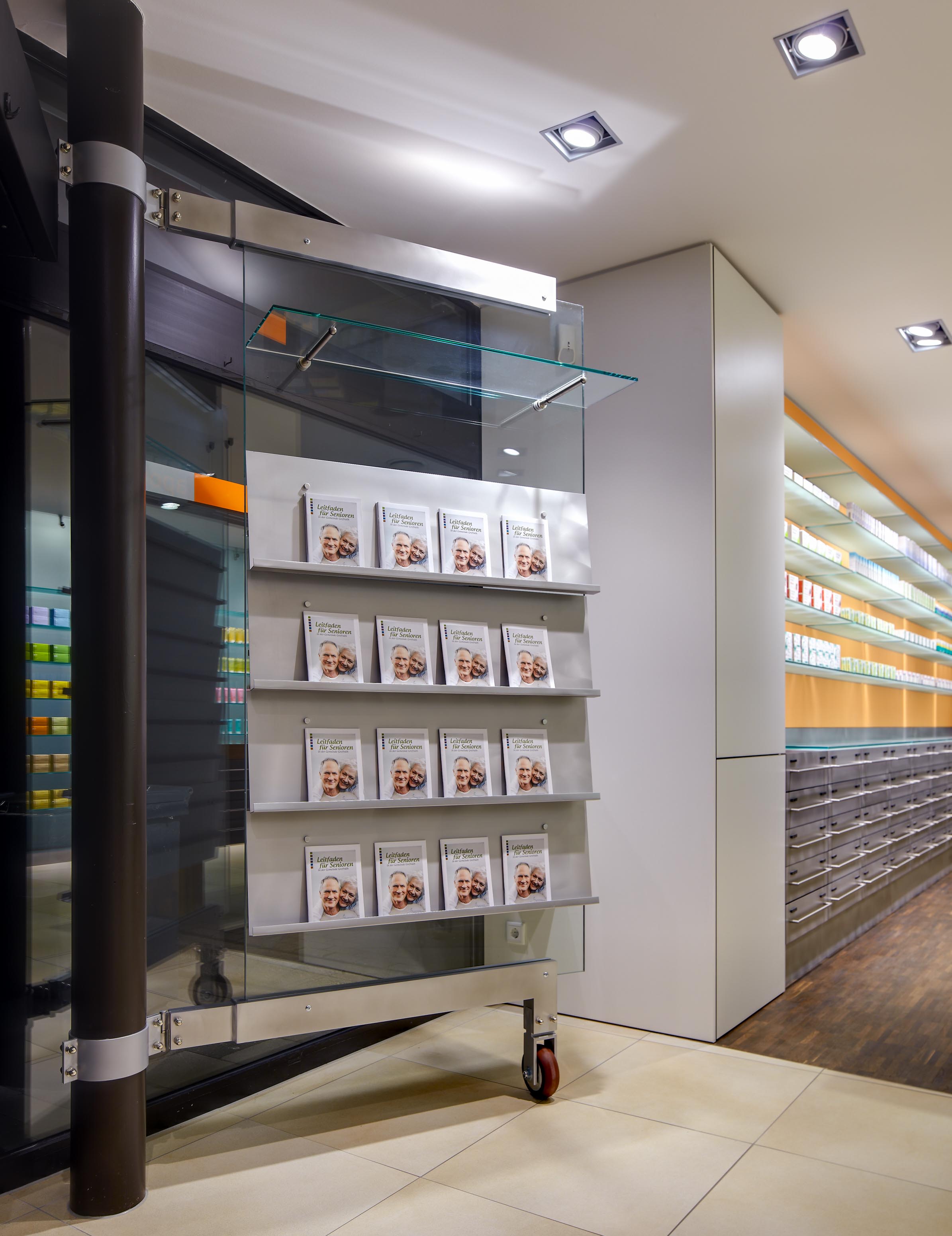 Prospektständer aus Edelstahl und Glas im Schaufensterbereich der Apotheke