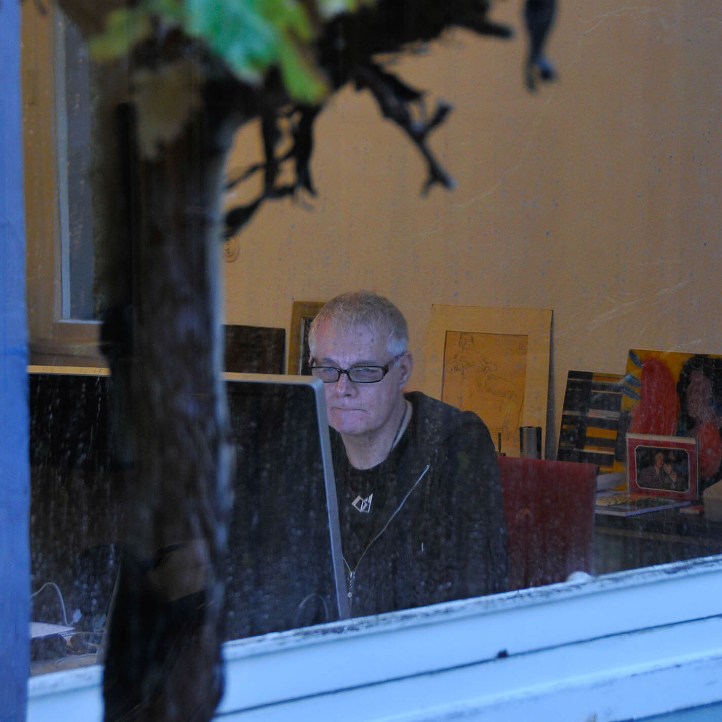 Architekt Klaus Bürger mit Brille bei der Arbeit am Bildschirm, Blick durch ein Fenster des Wintergartens